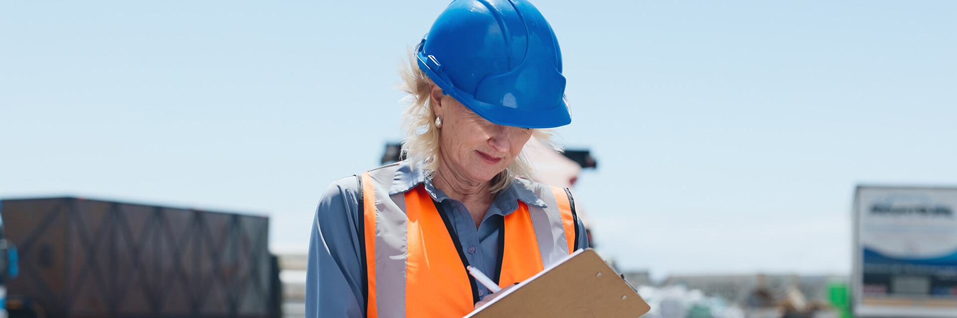 Frau mit Schutzweste und Helm schreibt auf einem Clipboard