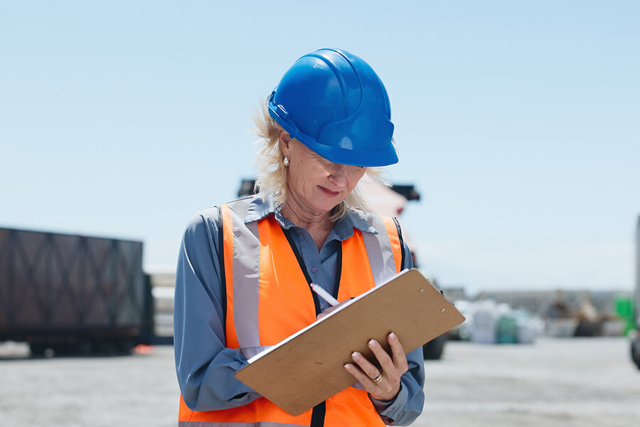 Frau mit Schutzweste und Helm schreibt auf einem Clipboard